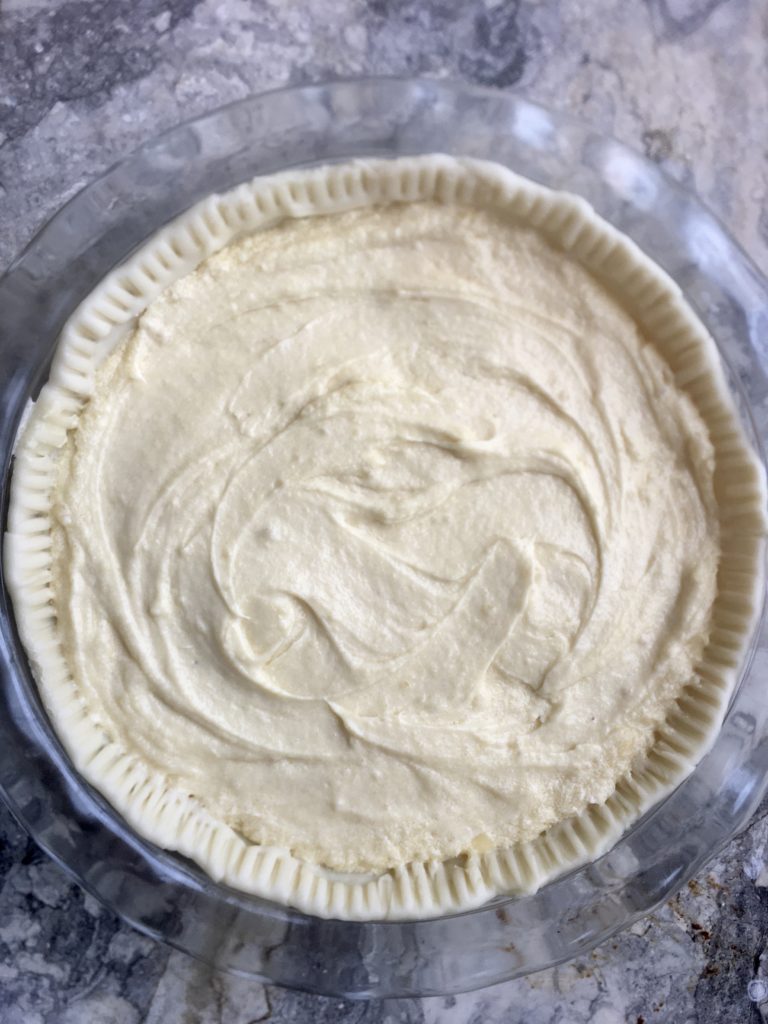 Ready for the oven: Unbaked piecrust in a heatproof glass pie pan, smoothed out into a thick flat filling, top down on marble countertop