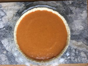 Before baking; crust in glass pie pan on marble countertop, filled with pumpkin spice egg evaporated milk mixture, ready for the oven. The before picture