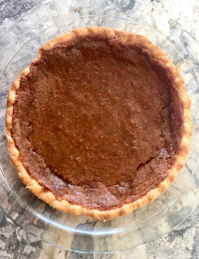 Classic Chess Pie, whole in glass pie pan on marble surface, handsome deep brown crackly surface