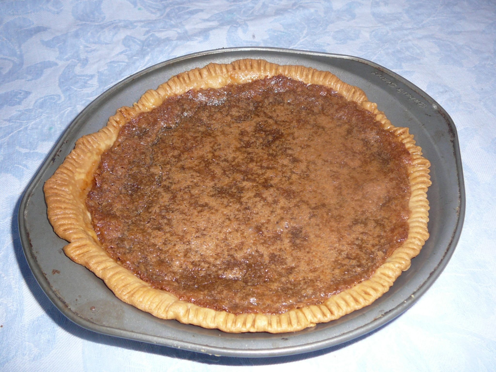 Classic Chess Pie in a metal pie pan, from above and back on a blue tablecloth