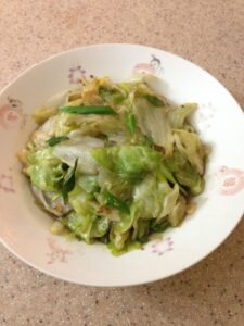 Stir fried lettuce in a deep serving plate, white with red designs on counter top