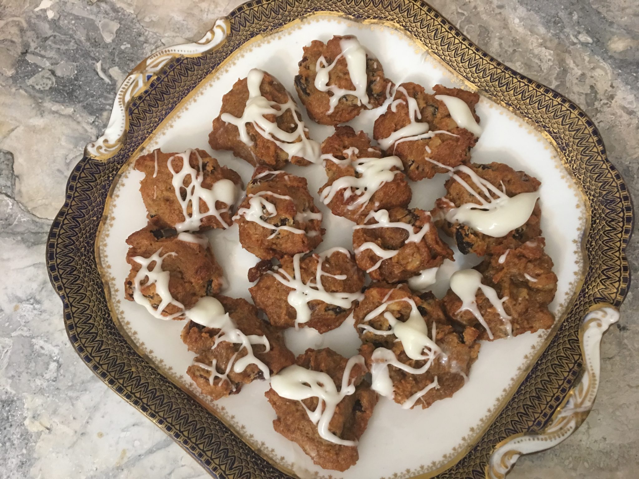 Plump persimmon cookies on a square white dessert plate with gold and navy trim, drizzled with white icing and set on a marble countertop