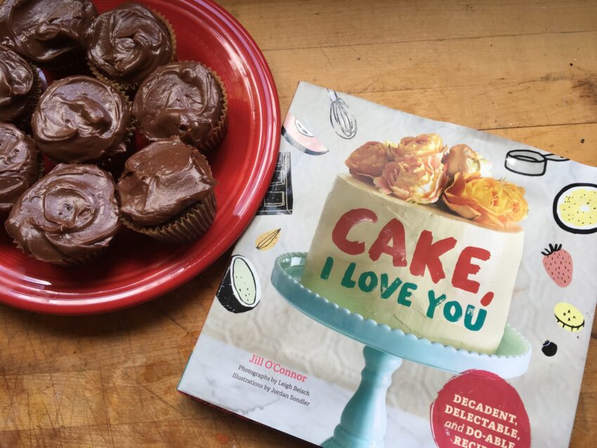 Eight rich chocolate cupcakes on a red plate next to a cover shot of "Cake I Love You" cookbook