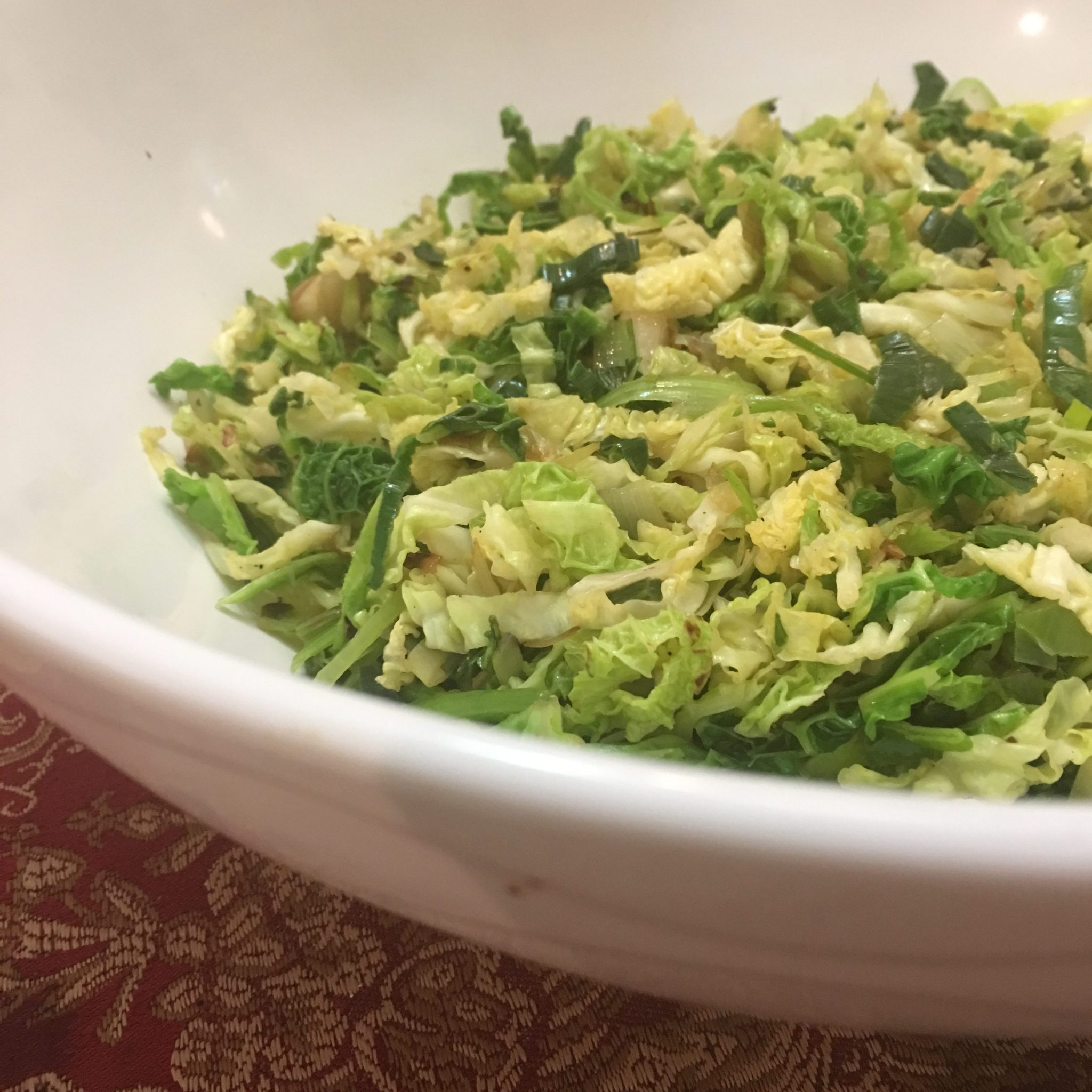 Big white ceramic bowl of sauteed leeks and cabbage, viewed from the side