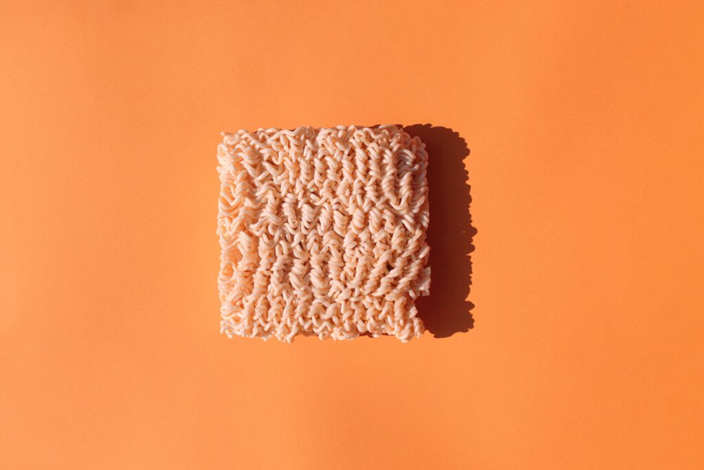 a square of ionstant noodles,uncooked, in the center of an orange surface