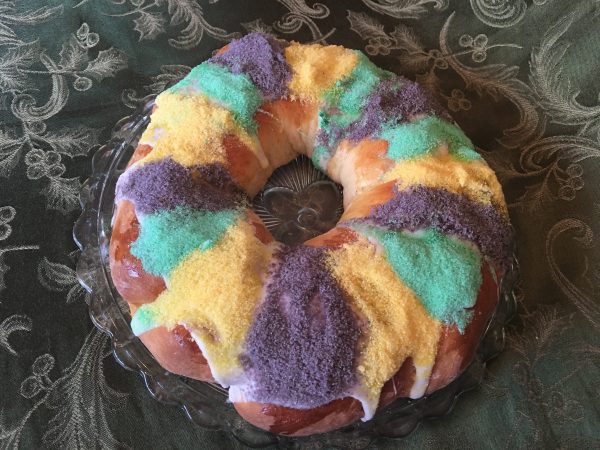 Whole Baked King Cake iced with purple, gold and green sugar decoration