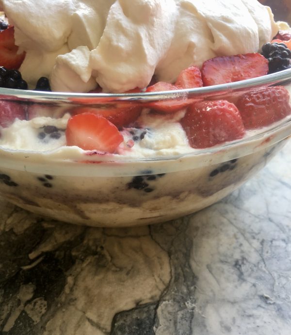 Sumemr berry trifle side view of big glass bowl, top layer shows clear strawberries and creamcovered blackberries plus big puffy topping cloud of sweetened whipped cream