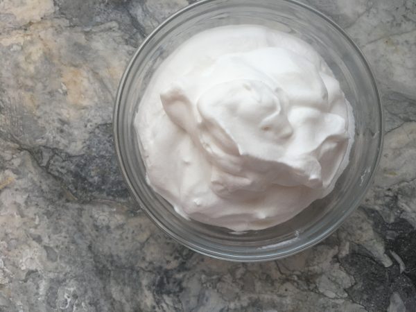 A small bowl full of fluffy, puffy cloud-like ethereal whipped cream, placed on a white marble countertop