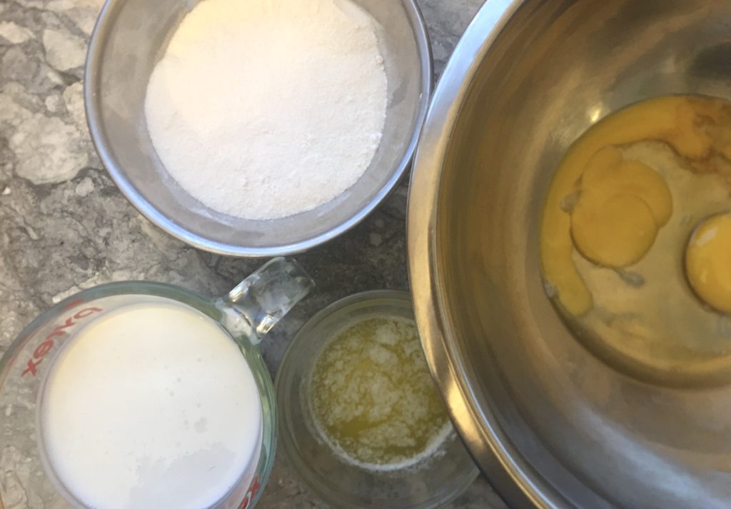Top down view of ingredients for buttermilk pie in bows on marble coutnertop, Eggs, sugar, vanilla, melted butter, and buttermilk.