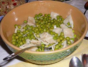 Big green ceramic mixing bowl full of green peas with dumplings; spoon in bowl and beside it