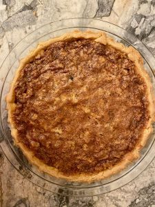top down view of Osgood Pie, a chess pie with raisins and pecans, pastry crust, glass pie pan on marble counter