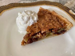 A piece of Osgood Pie on a white plate with whipped cream on the side and raisins adn pecans showing in the filling