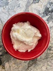 A pretty red bowl of whipped cream, lusciously piled up, placed on a marble slab