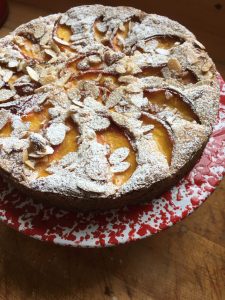 Peach Plum Cake on a red cake stand, top dusted with confectioner's sugar