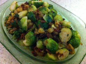 Brussels sprouts halved and cooked with bacon and apples in green depression glass bowl