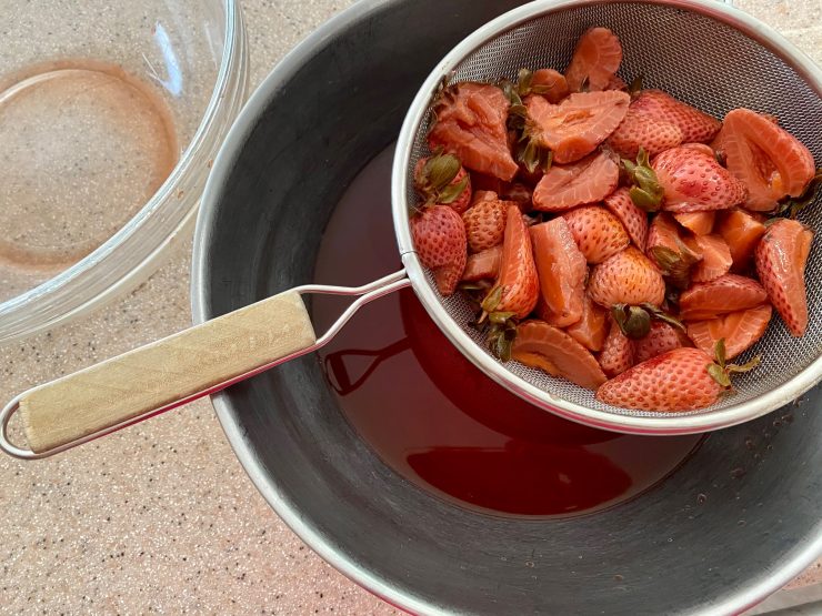 Straining out the strawberries, pouring the red fruity vinegar into a bowl to sweeten with sugar