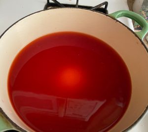 Strawberry vinegar with sugar added, barely visible in red liquid in ivory lined green Le Creuset dutch oven, ready for cooking to syrup; to become shrub!