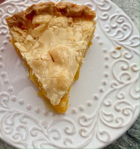 One piece of mango pie, double crust, on a white dessert plate with raised designs