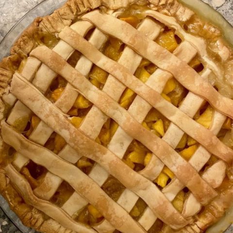 Fresh mango pie from above, with a quick-lattice top crust and and juicy filling peeking through, on a marble countertop