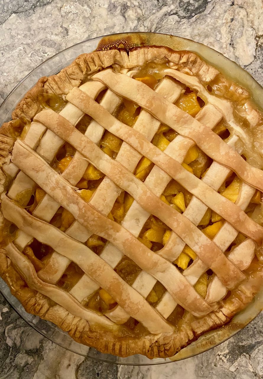 Fresh mango pie from above, with a quick-lattice top crust and and juicy filling peeking through, on a marble countertop