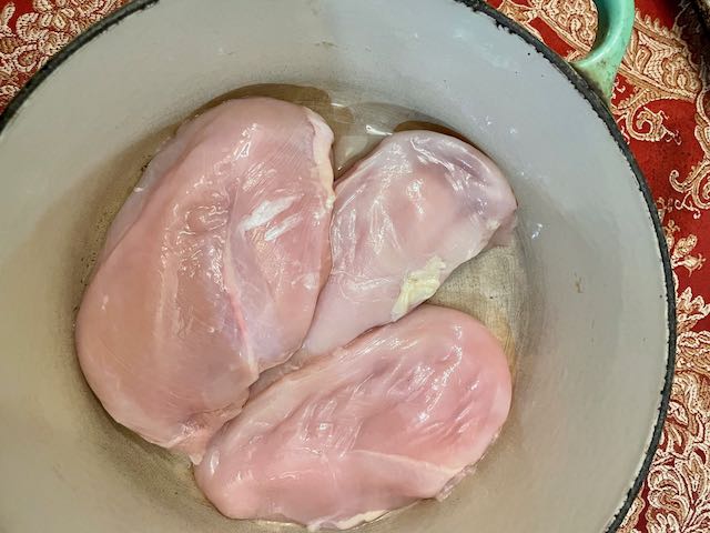 A big emamel cast iron pot with three plump chicken breasts in it, ready to cook. 