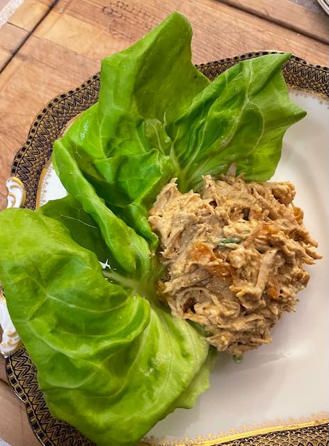 Generous scoop of curried luncheon treat: Coronation chicken salad with apricots on Boston lettuce leaf, white china with navy and gold trim on wooden counter