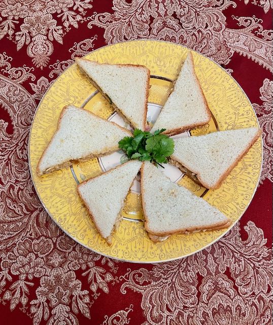 Triangles of chicken salad sandwiches, arranged on golden plates for a buffet.